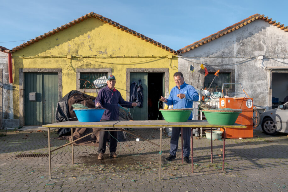 Fishermen preparing fish hooks in front of the warehouses.